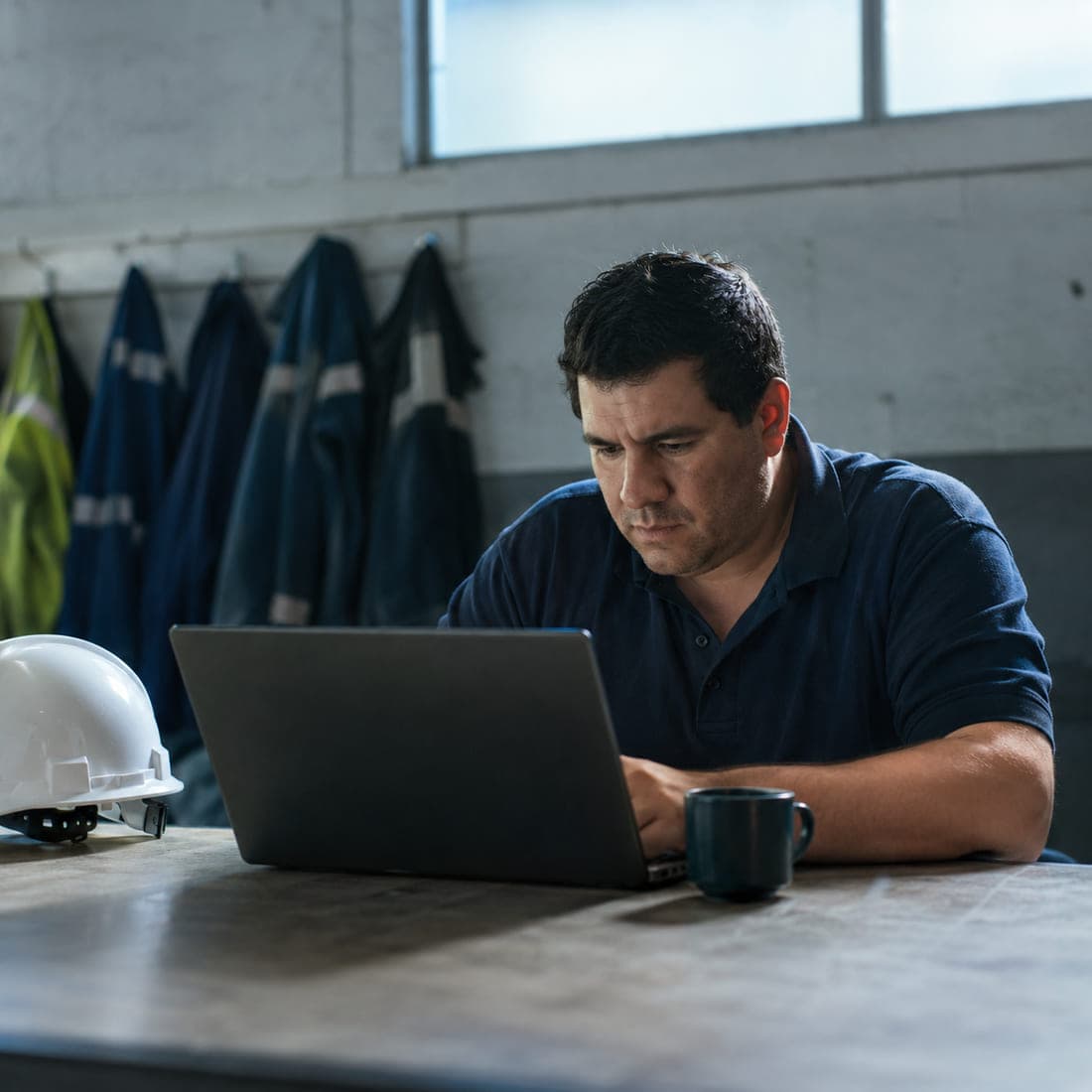 Trabajador siguiendo un curso en línea desde el comedor de la planta, con su casco sobre la mesa