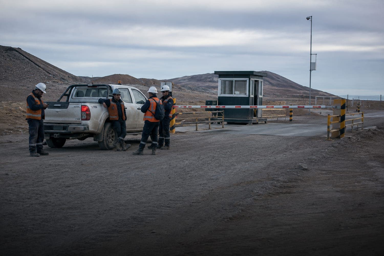 Cuatro trabajadores contratistas esperando junto a su camioneta en la barrera de acceso de una faena minera, temprano en la mañana